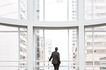 businessman standing looking out large white window of building lobby